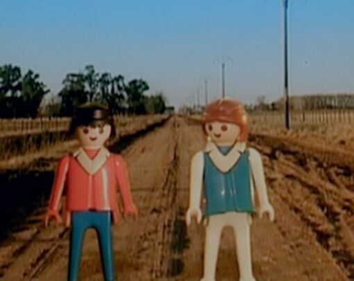 Dos playmobil que representan a dos personajes principales, sobre un fondo de un campo amarillo, con el cielo azul.