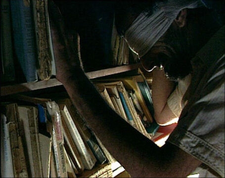 Fotograma de la película 76/.... Muestra al protagonista con una venda en la cabeza, inclinado hacia una estantería llena de libros.