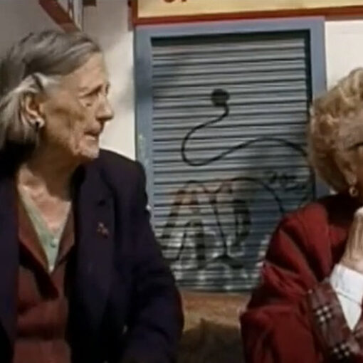 Dos vecinas del barrio sentadas en un banco y conversando.