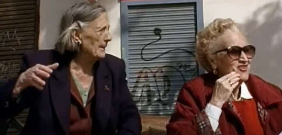 Dos vecinas del barrio sentadas en un banco y conversando.