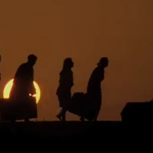Siluetas de personas caminando cargadas con equipaje, con el sol de fondo.