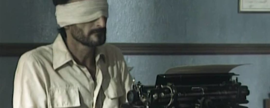 Fotograma de la película 76/... Se ve a un hombre con los ojos tapados por una venda escribiendo en una maquina de escribir.