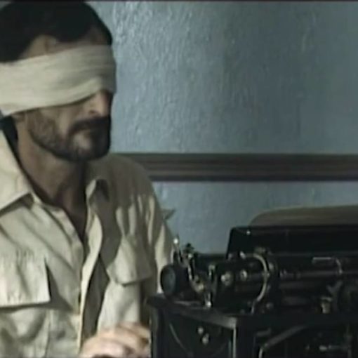 Fotograma de la película 76/... Se ve a un hombre con los ojos tapados por una venda escribiendo en una maquina de escribir.