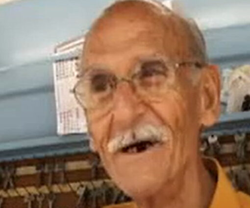 Un hombre mayor sonríe. Al fondo, hay un estante lleno de llaves.