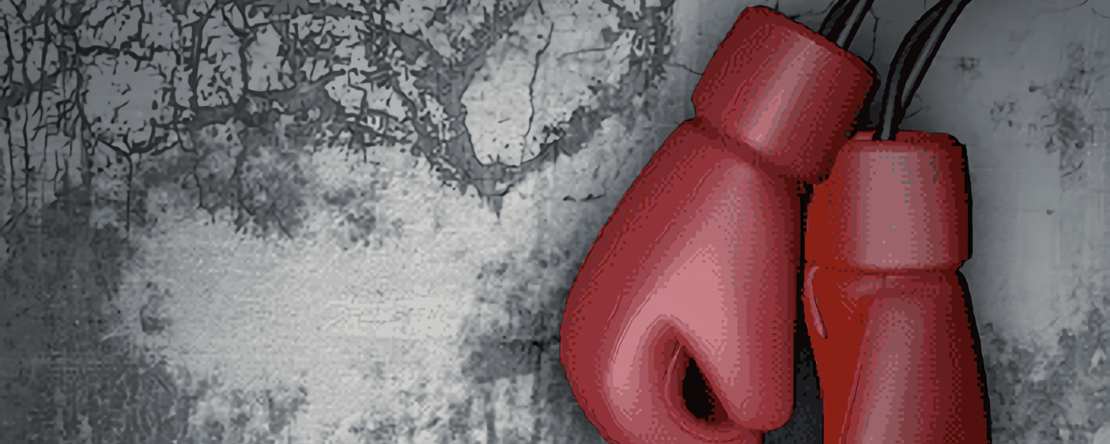 Guantes de boxeo rojos colgados frente a una pared gris agrietada.