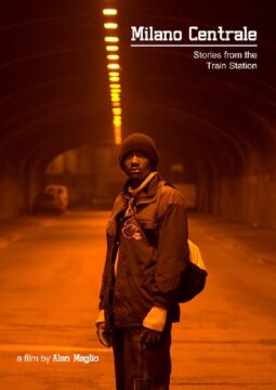 Cartel del documental Milano Centrale: Stories from the Train Station. Muestra a un hombre de pie en un túnel iluminado con luz naranja, con expresión seria y una mochila al hombro