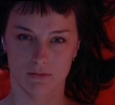 Rostro inexpresivo de una mujer tumbada sobre un colchón rojo.