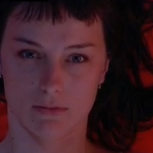 Rostro inexpresivo de una mujer tumbada sobre un colchón rojo.