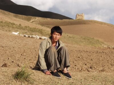 Chico joven de rasgos oruentales sentado en un campo terroso.