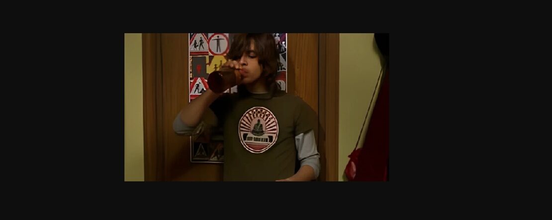 Adolescente con cabello largo y camiseta verde bebe de una botella en una habitación. Detrás de él, hay una puerta decorada con pósters de señales de tránsito.