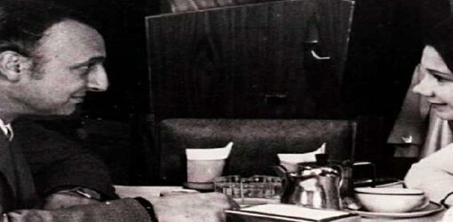 Hombre y mujer conversan sentados frente a frente en una mesa de café, en una escena en blanco y negro.