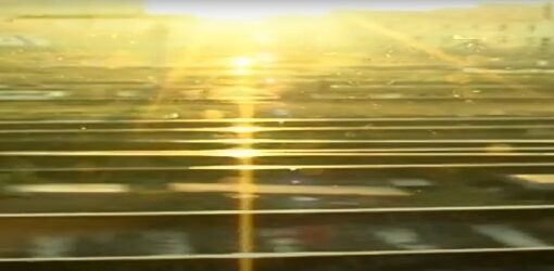 Vista desde una ventana hacia unas vías de tren al amanecer o atardecer. La luz del sol brilla intensamente en el horizonte