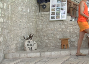 Fotograma de "No olvidar, voces más allá del olvido". Calle de peidra. En un pequeo altar de piedra, una roca con un grabado: "Don't forget '93". 
