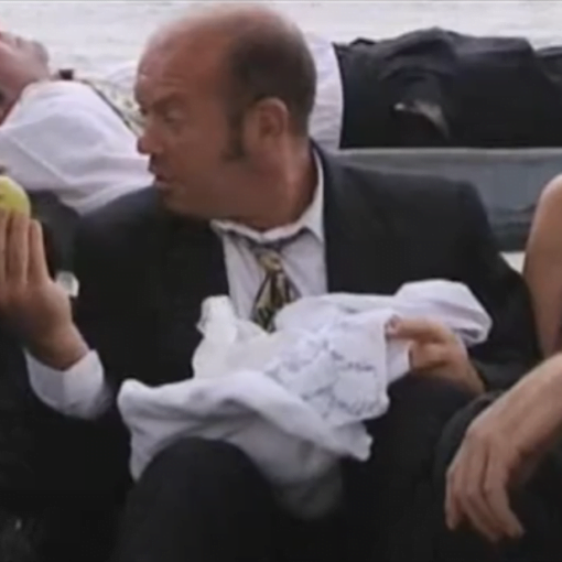 Hombres en traje y una mujer sentados, uno de los hombres sostiene una manzana y otro un pañuelo blanco.