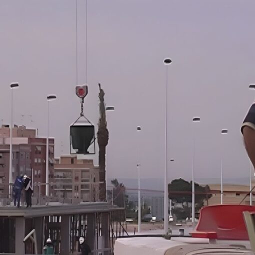 Hombre canoso en la azotea mirando a trabajadores y grúa en un sitio de construcción urbano al atardecer.