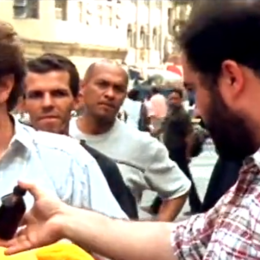 Fotograma de "Trucos, jarabes y otros artículos de confianza". Un vendedor le ofrece jarabe al otro vendedor de peluches en medio de la plaza entre barullo de gente. Miden la confianza.