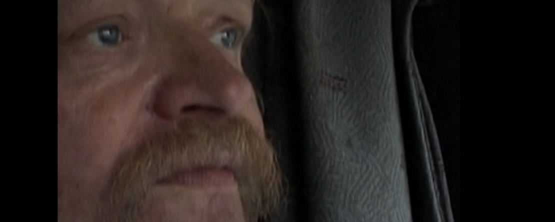 Primer plano del rostro de Bertil, un camionero de mediana edad con bigote y mirada fija, observado en silencio mientras conduce, reflejando introspección y el paso del tiempo durante sus largas horas en la carretera.