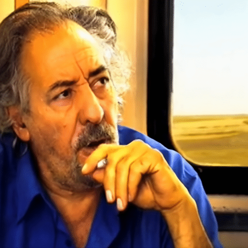 Hombre sentado en un tren, mientras sostiene un cigarro con rostro pensativo