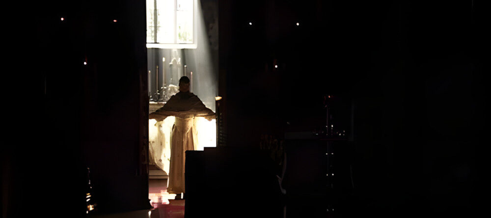 Fotograma de "Vista desde el puente: Historias de Kosovo" - Figura en el umbral de una iglesia bañada por un rayo de luz.