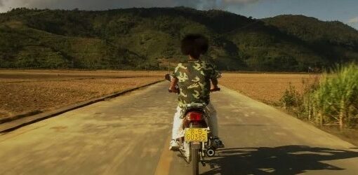 Fotograma de la película A través de la montaña. En la imagen se ve una persona, sentado en una moto, en medio de la carretera.