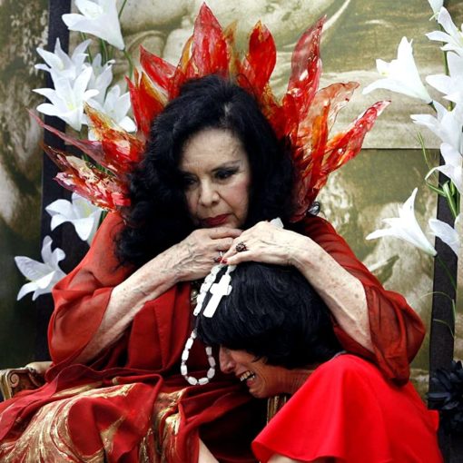 Una mujer con vestido rojo y pelo negro está sentada y mira hacia el suelo.