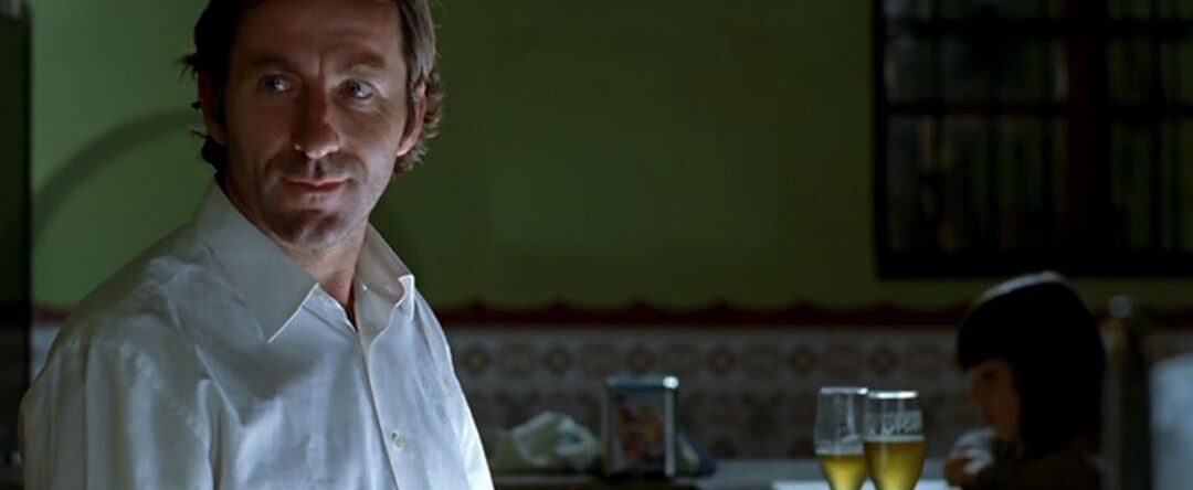 Fotograma del corto Una caja de botones en el que aparece el protagonista vestido con una camisa blanca. Está en un bar detrás de él hay una niña leyendo sobre la barra.