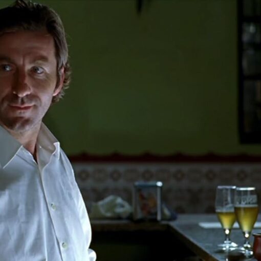 Fotograma del corto Una caja de botones en el que aparece el protagonista vestido con una camisa blanca. Está en un bar detrás de él hay una niña leyendo sobre la barra.