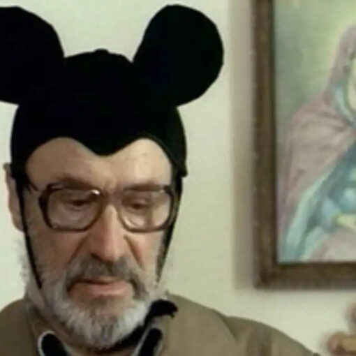 Niki y Flo. Fotograma del largometraje. Se ve a un hombre mayor que a pesar de su porte serio, tiene puesto un gorro de Mickey Mouse.