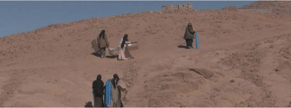 Fotograma del documental en el que aparecen cuatro mujeres cargadas con fardos que caminan por el desierto.