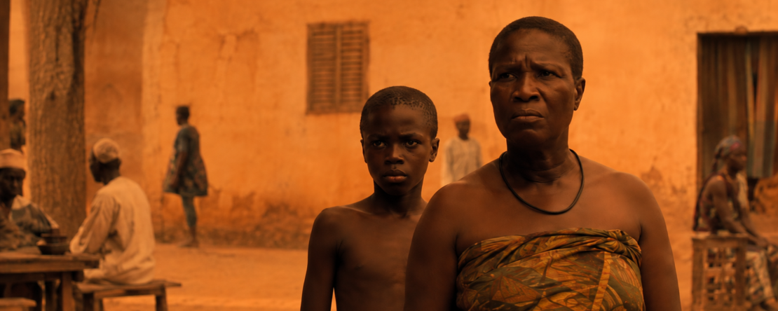 Mujer y niño en un patio africano, con una ambientación cálida y tonos anaranjados.