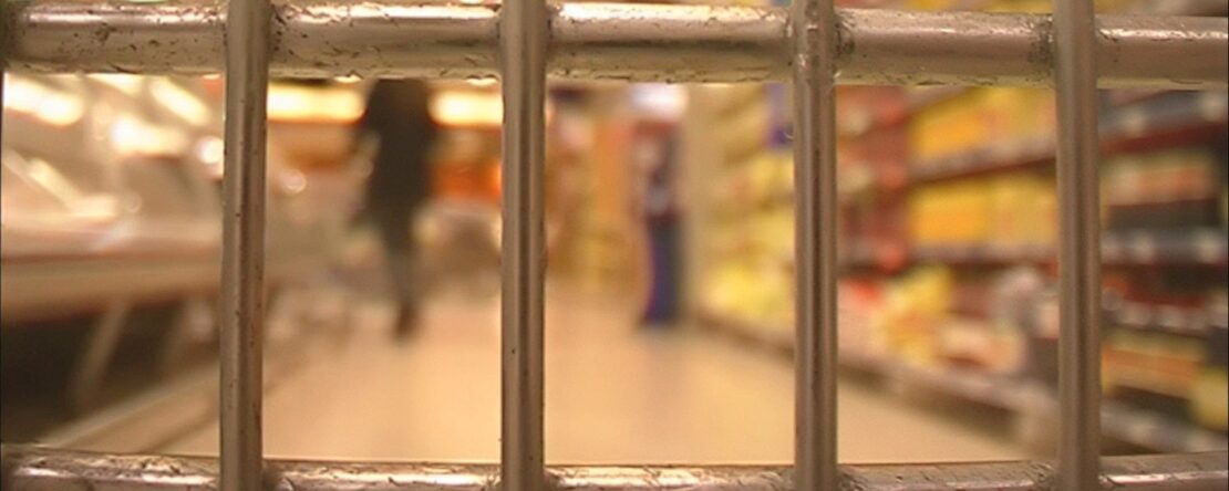 Imagen de primer plano de las rejas de un carro de la compra que simulan unas rejas, desenfocado de fondo se ve el interior de un supermercado