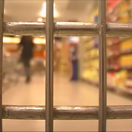 Imagen de primer plano de las rejas de un carro de la compra que simulan unas rejas, desenfocado de fondo se ve el interior de un supermercado