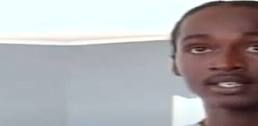Primer plano de un hombre joven hablando, con expresión seria, en una habitación de paredes grises.
