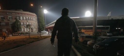 Un hombre de espaldas, está caminando en una ciudad. La luz proviene de las farolas, que están encendidas en la noche.