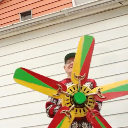 En primer plano, un hombre sostiene una hélice decorada por él con colores rojo, verde y amarillo.