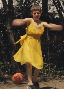 Un chico con un vestido amarillo puesto es rubio y esta bailando encima del cesped