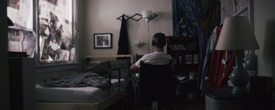 Fotograma del cortometraje "El agujero" en el que el protagonista está en su habitación sentado en una silla escuchando música. De espaldas a la cámara.