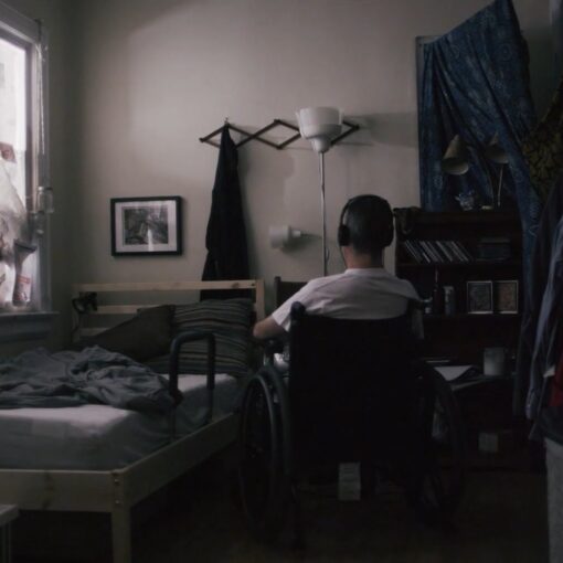 Fotograma del cortometraje "El agujero" en el que el protagonista está en su habitación sentado en una silla escuchando música. De espaldas a la cámara.