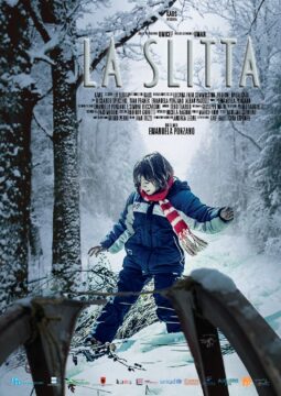 Cartel de la película "La Slitta", que muestra a un niño con abrigo azul y bufanda roja caminando por un bosque nevado. En primer plano se ve parte de un trineo y al fondo árboles cubiertos de nieve.