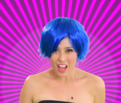 Fotograma de "Poesía y Melodía". Dos niñas a los lados y una mujer con peluca azul en el centro, sobre fondo morado, cantan y bailan