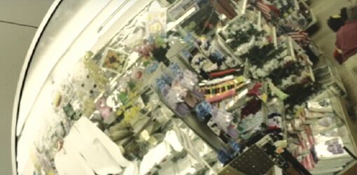 Espejo de seguridad que muestra el interior de una tienda con estantes llenos de productos. Dos niños estan subidos a un carrito de la compra