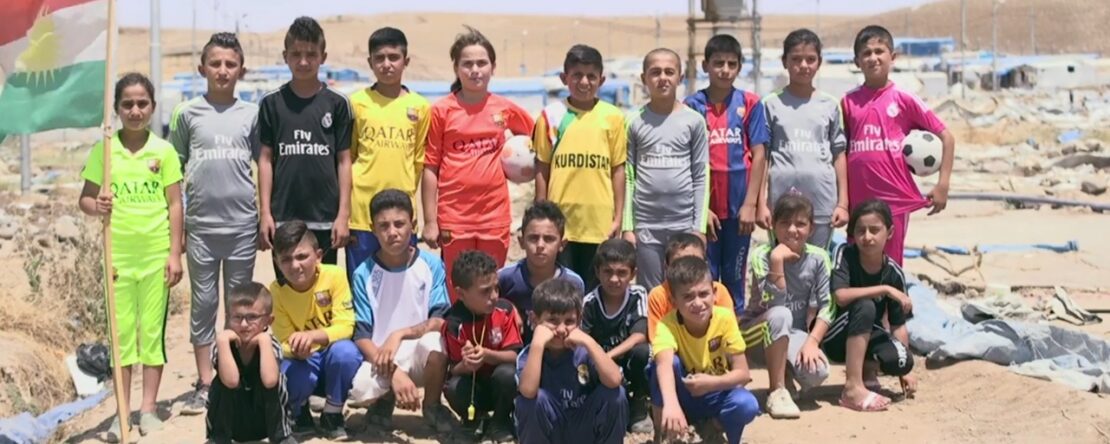 Un grupo de niños y jóvenes posa al aire libre con camisetas de fútbol de diversos equipos, algunos sosteniendo una bandera.