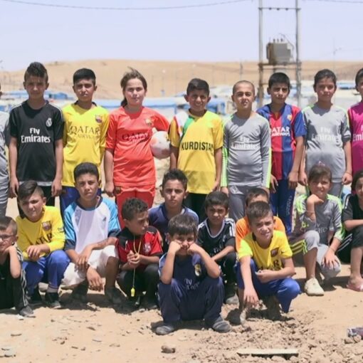 Un grupo de niños y jóvenes posa al aire libre con camisetas de fútbol de diversos equipos, algunos sosteniendo una bandera.
