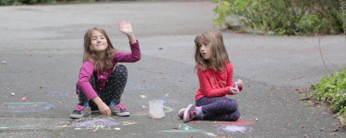 Alberto. Fotograma de la película. Se ve a dos niñas jugando en la calle, haciendo pintadas en el suelo con lápices de colores.