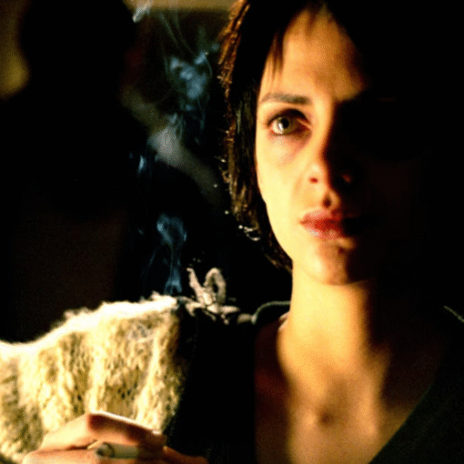 Mujer joven con expresión seria sosteniendo un cigarrillo encendido en un ambiente oscuro.