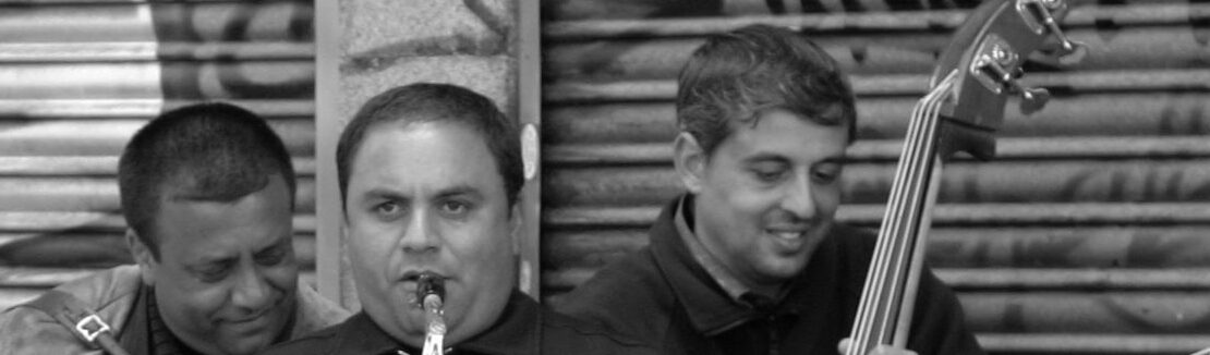 Grupo de hombres, con gesto alegre, tocando instrumentos en la calle. Foto en blanco y negro.