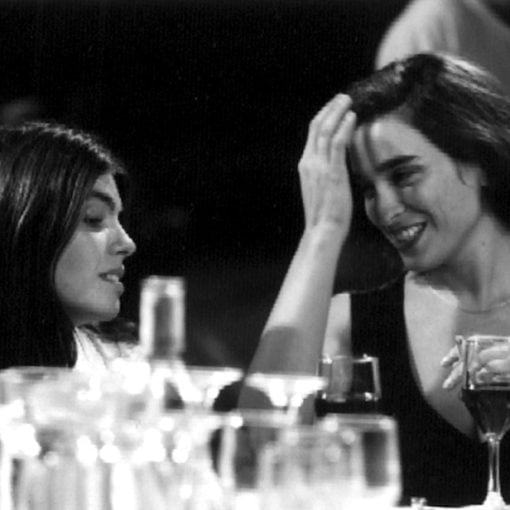 Dos mujeres, que están sentadas, charlan mientras cenan. Iluminación en blanco y negro.
