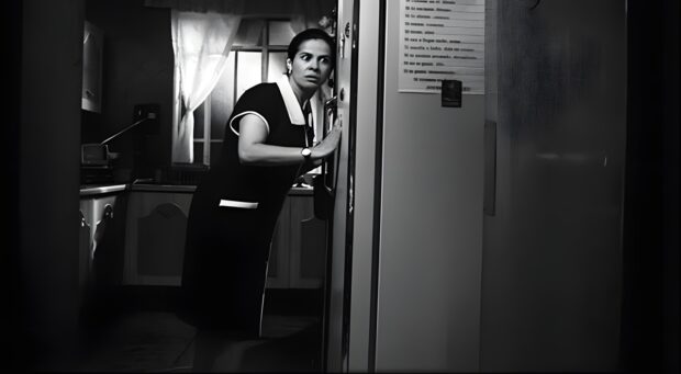 Mujer con un vestido negro con detalles blancos en el cuello mirando con expresión de sorpresa desde el umbral de una cocina.