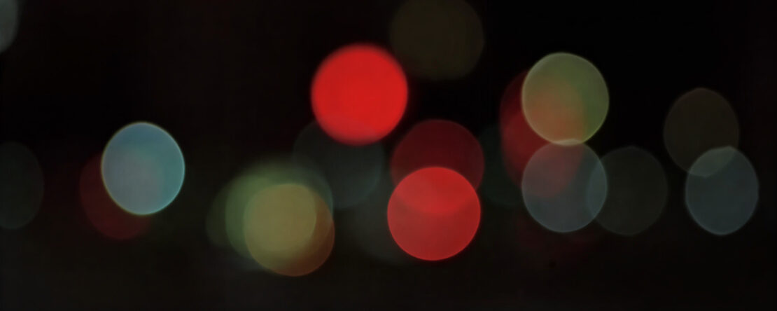 Luces de la ciudad desenfocadas sobre un plano negro, recuerdan a las luciérnagas en la noche.