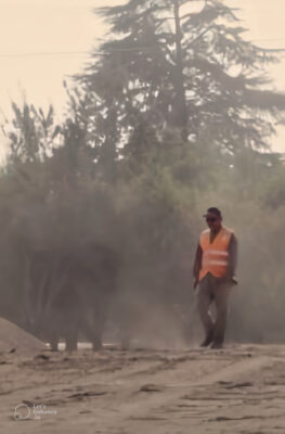 Trabajador con chaleco reflectante caminando por un terreno polvoriento al aire libre.
